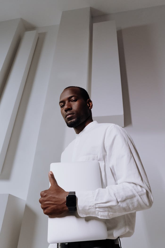 Professional African American man holding a laptop confidently in a modern office setting.